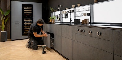 Monteur installeert lade in rechte keuken met houten fronten, wijnklimaatkast en accessoires