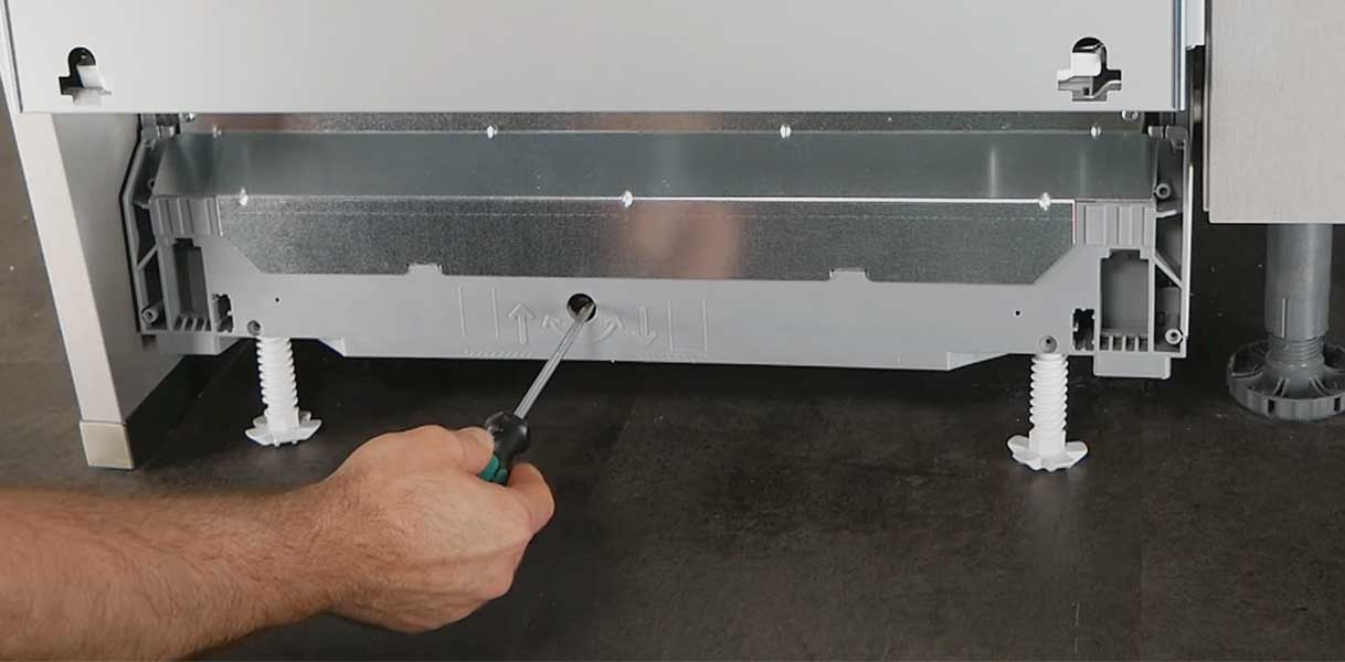 Monteur stelt vaatwasser waterpas af met schroevendraaier aan de voorzijde.