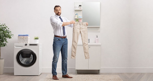 Man toont gekrompen jeans bij droger met risico op pasvormverlies en vervaagde kleuren