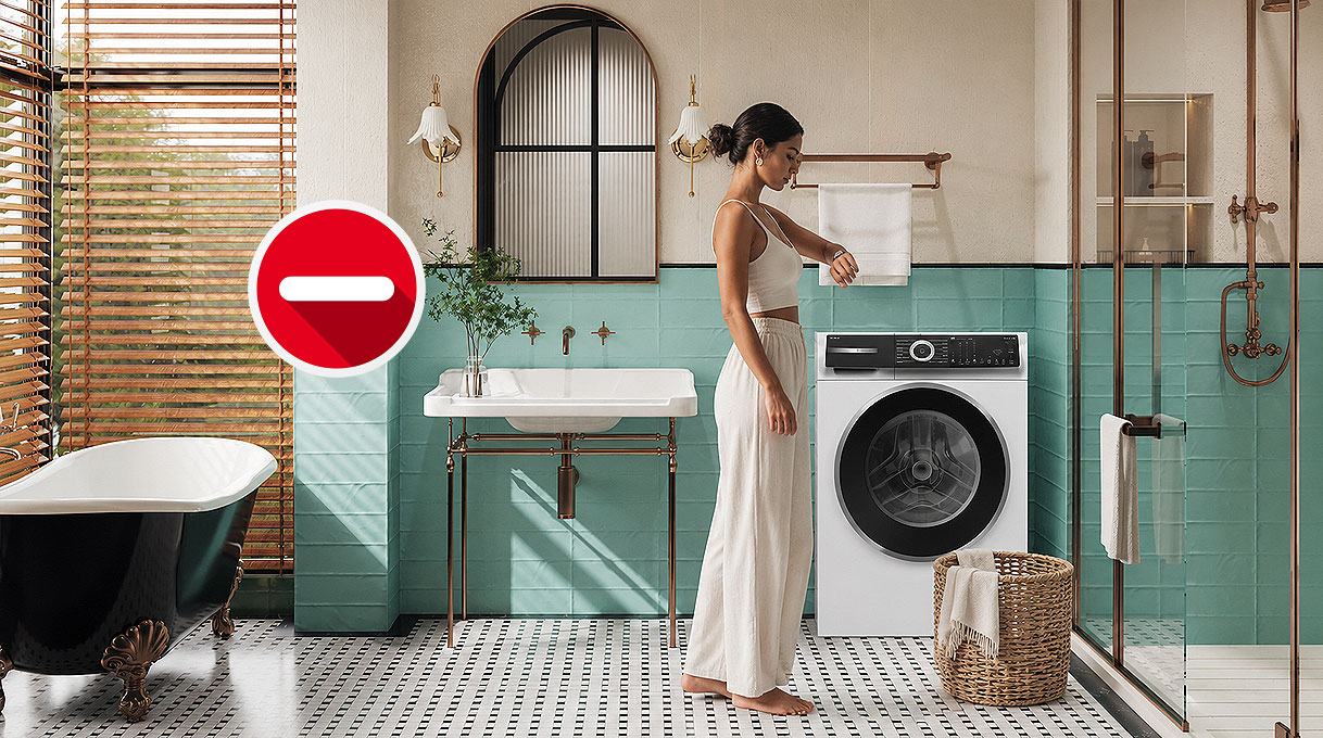Vrouw bekijkt een handdoek naast een wasmachine met stoomfunctie in een badkamer