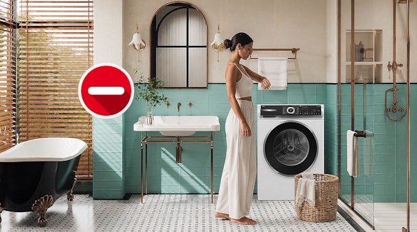 Vrouw bekijkt een handdoek naast een wasmachine met stoomfunctie in een badkamer