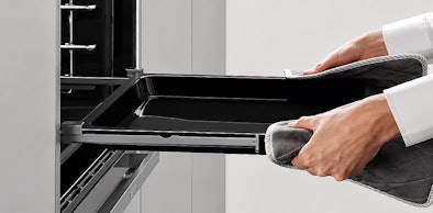 Bakplaat op volledig uitgeschoven cliprails uit de NEFF oven trekken met ovenwanten