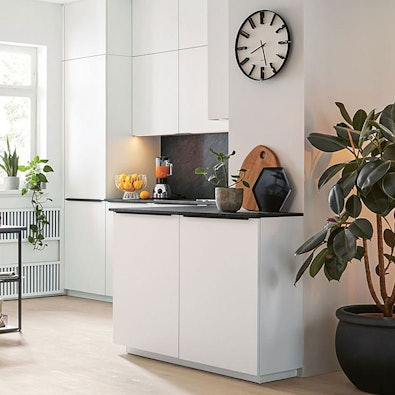 Moderne keuken met witte kasten, licht werkblad en planten, ingericht in neutrale kleuren voor een rustige en tijdloze uitstraling.