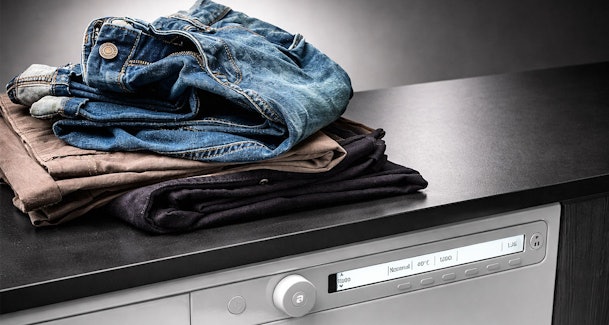 Stapels jeans en donkere kleding op Asko wasmachine met normaal wasprogramma actief