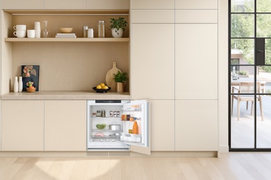 Onderbouw koelkast in lichte keuken, geïntegreerd onder het werkblad met open deur en compacte indeling.