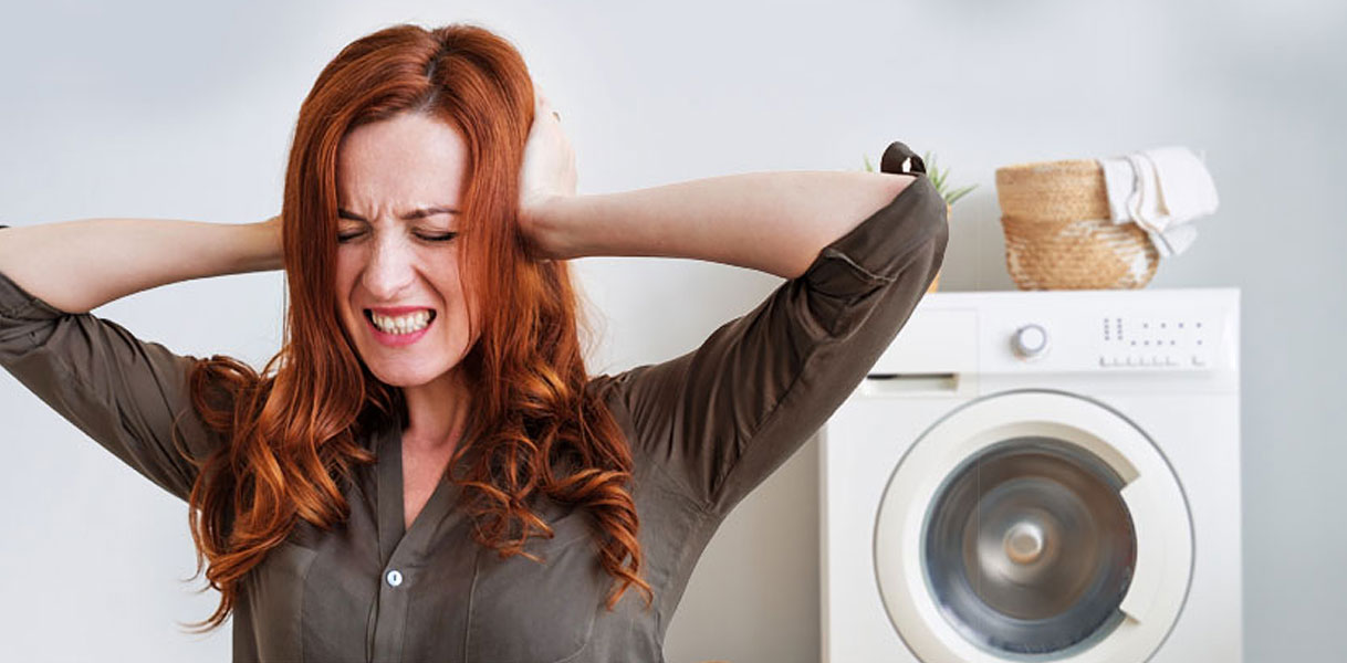 Vrouw houdt haar handen op haar oren naast een draaiende wasmachine