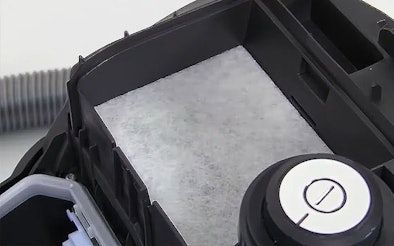 Geopend filtercompartiment van een sledestofzuiger met zichtbaar wit motorfiltervlies, klaar om de oude filter voorzichtig te verwijderen zonder stof te verspreiden.