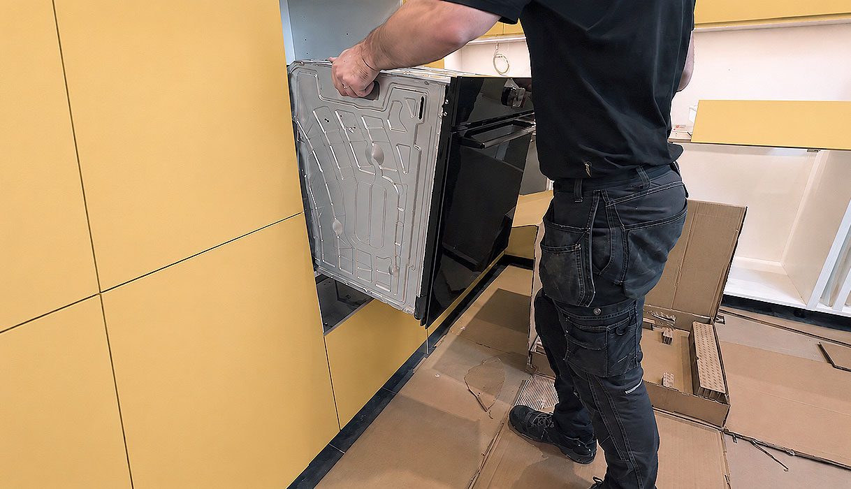 Monteur schuift een oven in een keukenkastje tussen verpakkingsmateriaal op de vloer