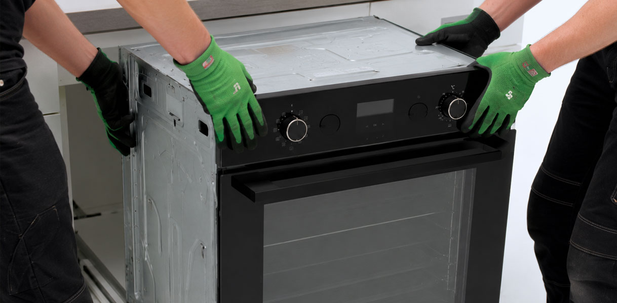 Twee personen met werkhandschoenen trekken samen een oven naar voren uit de keukenkast