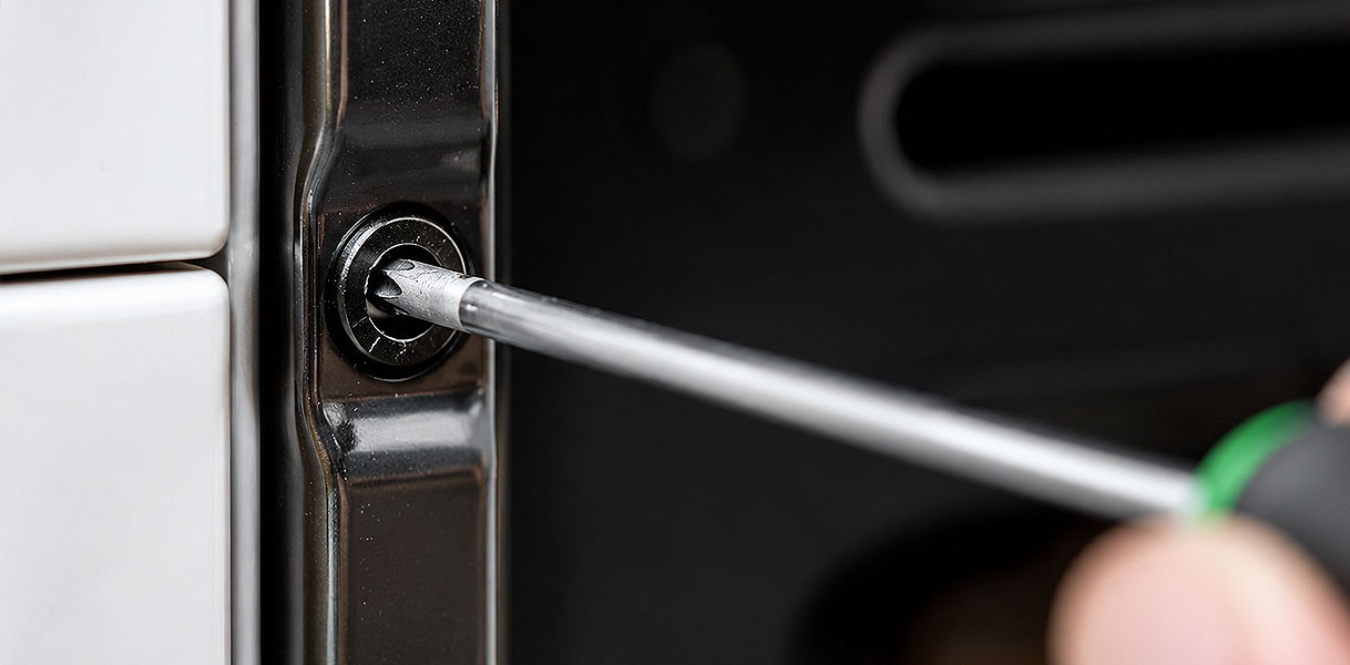 Schroevendraaier draait de meegeleverde schroef vast in de deuropening van de geplaatste oven