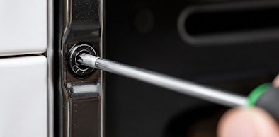 Schroevendraaier draait de meegeleverde schroef vast in de deuropening van de geplaatste oven