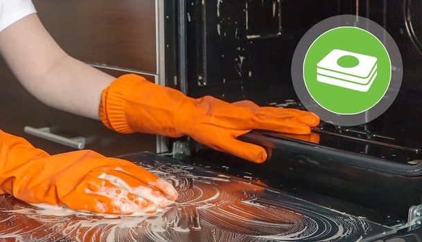 Oven worden gereinigd met schuim terwijl iemand met oranje schoonmaakhandschoenen het oppervlak afneemt