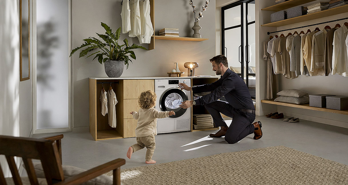 Man met kind laadt premium Miele warmtepompdroger van 9 kg in moderne wasruimte