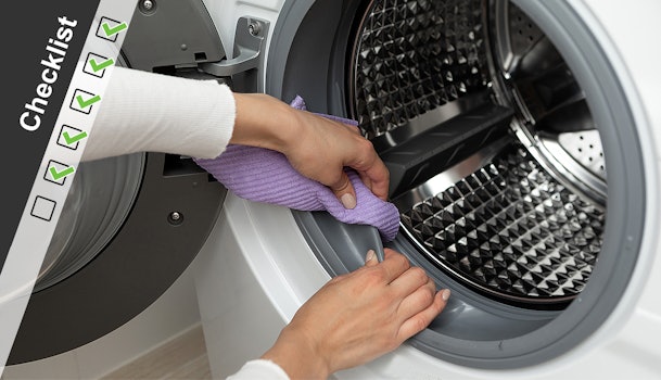 Handen reinigen de rubberen manchet van een wasmachine met een paarse doek, met checklist-icoon in beeld