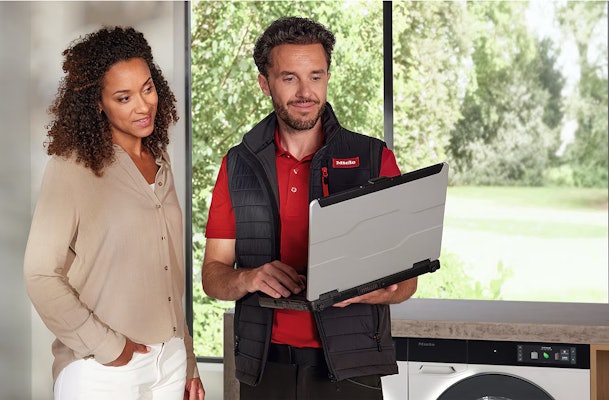 Miele servicemonteur met laptop diagnosticeert wasmachine storing bij klant thuis
