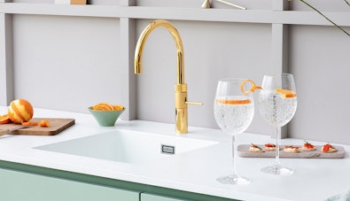 Gouden Quooker Fusion Round kraan met twee glazen bruisend water en sinaasappel
