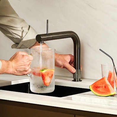 Quooker Front Gunmetal met bedieningsknop aan de voorzijde — bruisend water wordt getapt in glazen karaf