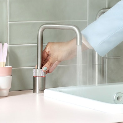 Quooker Nordic RVS met lichtring — hand bedient de draaiknop terwijl kokend water uit de kraan stroomt