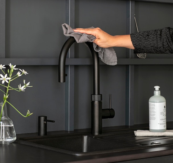 Zwarte Quooker Fusion Round wordt schoongemaakt met zachte doek in donkere keuken