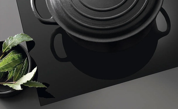 Miele inductiekookplaat met elegante randlijst en zwarte kookpan met verse kruiden