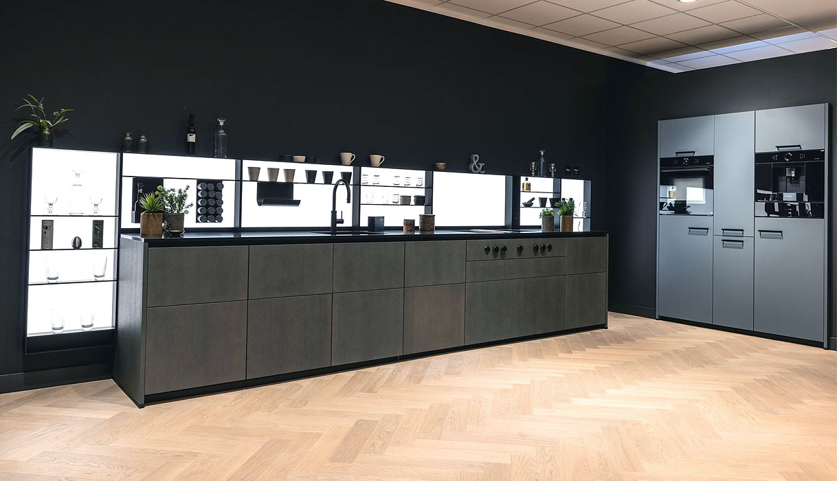 Moderne rechte keuken zonder bovenkastjes met donkere fronten, verlichte achterwand en losse hoge kasten in een ruim interieur.