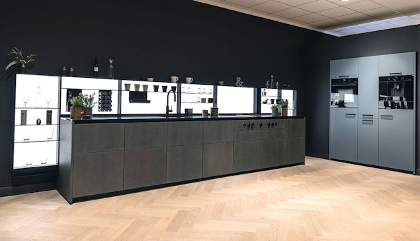 Moderne rechte keuken zonder bovenkastjes met donkere fronten, verlichte achterwand en losse hoge kasten in een ruim interieur.