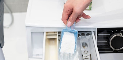 Hand giet waspoeder met een maatschepje in het zeepbakje van een wasmachine