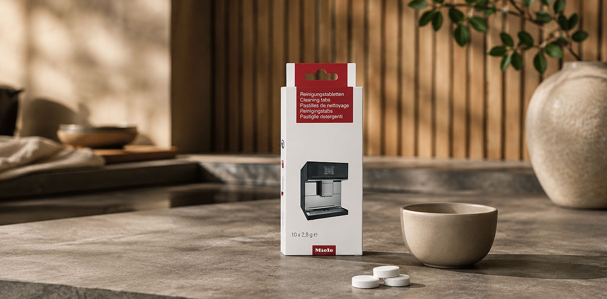 Verpakking Miele reinigingstabletten naast een inbouw koffiemachine en een koffiekop