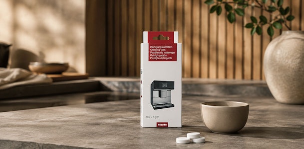 Verpakking Miele reinigingstabletten naast een inbouw koffiemachine en een koffiekop
