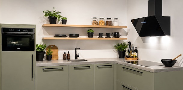 Scandinavische keuken met saliegroene onderkasten, licht houten wandplanken en keramisch werkblad