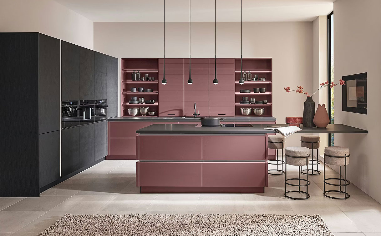 Roze schiereiland als ruimteverdeler tussen keuken en woonkamer in een open woonkeuken met barkrukken aan de woonkamerzijde