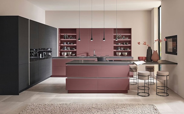 Roze schiereiland als ruimteverdeler tussen keuken en woonkamer in een open woonkeuken met barkrukken aan de woonkamerzijde