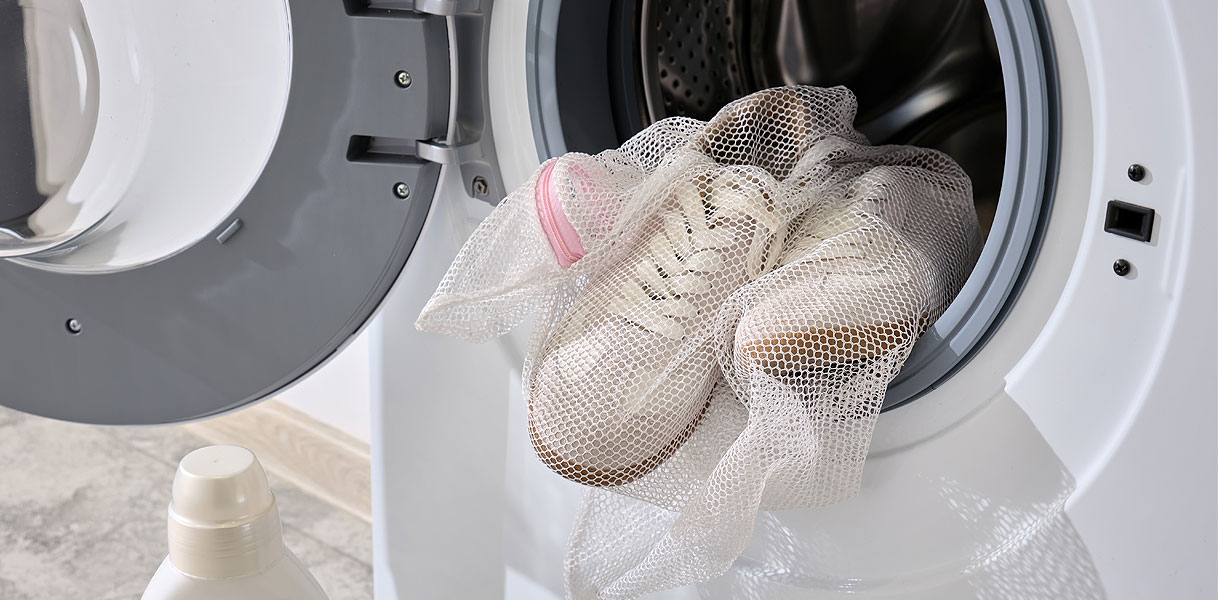 Witte sneakers in een waszakje worden in de wasmachine geplaatst, met een fles wasmiddel ernaast