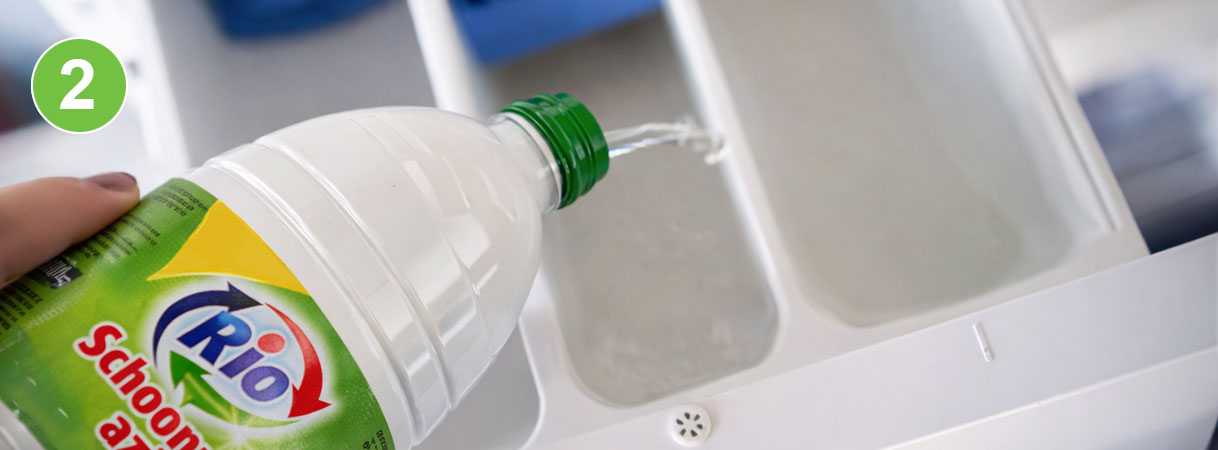 Schoonmaakazijn toevoegen aan wasmachine: fles Rio schoonmaakazijn wordt uitgegoten in het wasverzachterbakje van de wasmachine