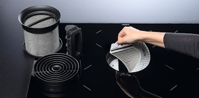 Hand vervangt koolstoffilter van downdraft afzuigkap met vetfilter ernaast