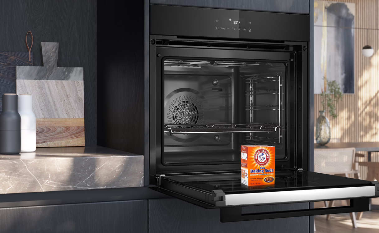 Open oven met een doos baking soda op de ovendeur, klaar voor een veilige schoonmaakbeurt