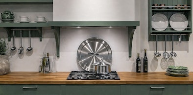 Decoratieve schouw boven gaskookplaat met houten werkblad, kookgerei en serviesgoed in landelijke keuken