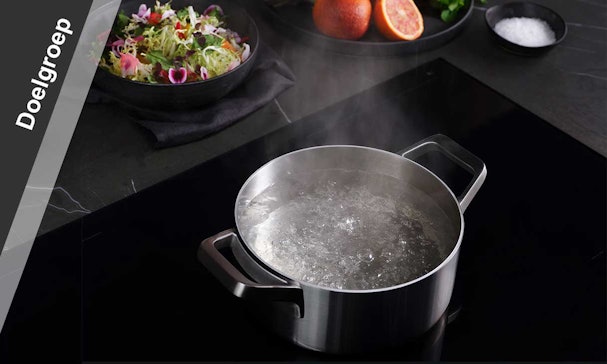 Kokend water in pan op inductiekookplaat met salade op achtergrond