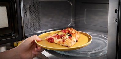 Hand plaatst bord met pizza in Whirlpool magnetron met SensorCooking functie voor automatische bereiding