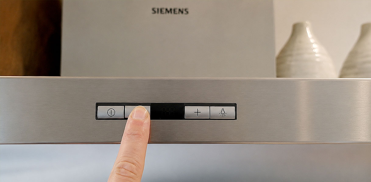 Vinger drukt op de bedieningsknoppen van een Siemens afzuigkap om de filterindicatie te resetten