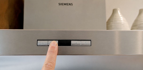 Vinger drukt op de bedieningsknoppen van een Siemens afzuigkap om de filterindicatie te resetten