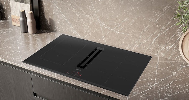 Siemens iQ300 inductiekookplaat met geïntegreerde afzuiging ingebouwd in een donker keukenblad