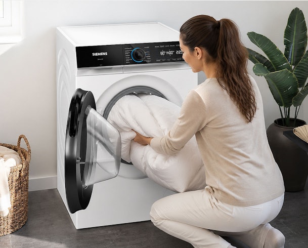 Vrouw laadt een tweepersoons dekbed in de trommel van een Siemens wasmachine van 10 kg