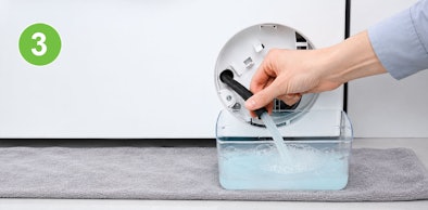 Water loopt via de losgedraaide afsluitdop van een Siemens wasmachine in een platte bak