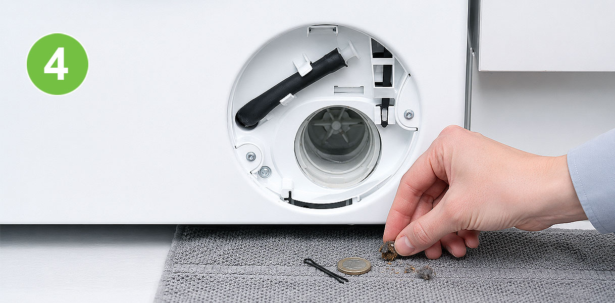 Hand haalt een muntje en vuil uit het geopende pomphuis van een Siemens wasmachine