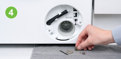 Hand haalt een muntje en vuil uit het geopende pomphuis van een Siemens wasmachine