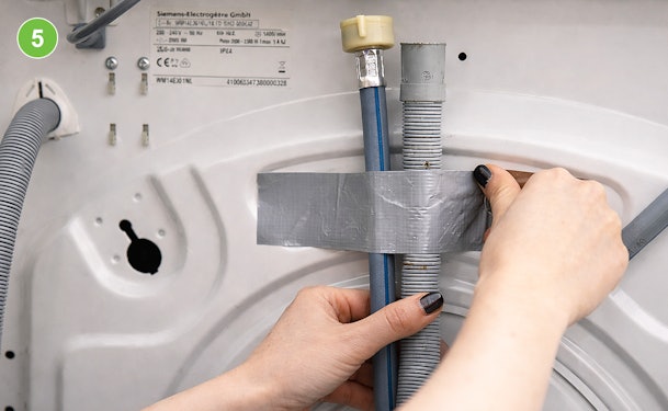 Toevoer- en afvoerslang van een wasmachine vastgezet met ducttape aan de achterkant