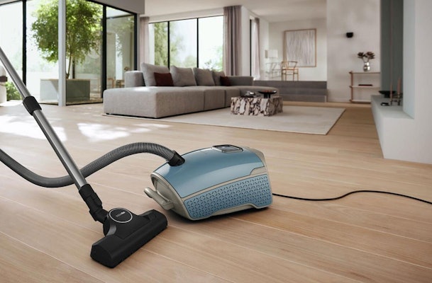 Miele sledestofzuiger op houten vloer in moderne woonkamer met zuigslang en mondstuk