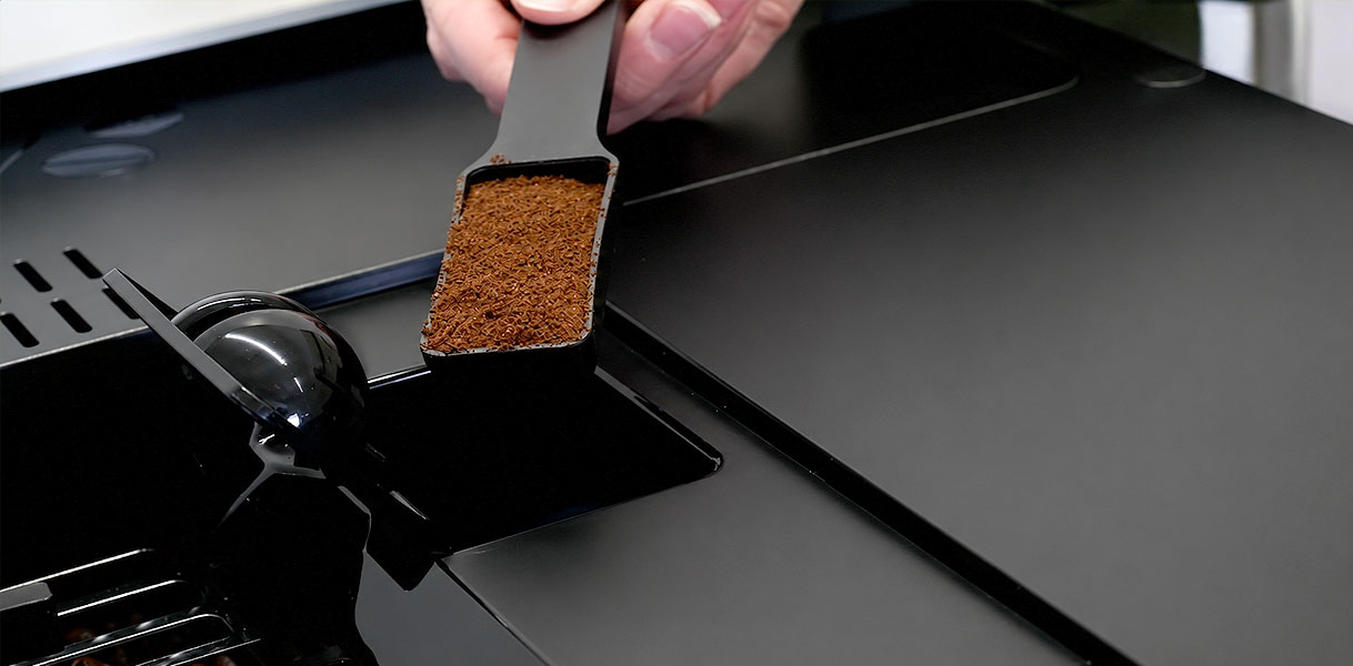 Maatschep met gemalen koffie boven het aparte vak van een SMEG koffiemachine