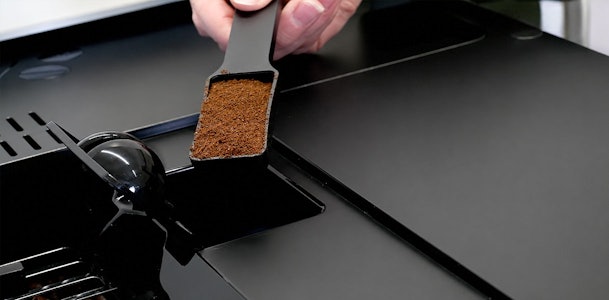 Maatschep met gemalen koffie boven het aparte vak van een SMEG koffiemachine